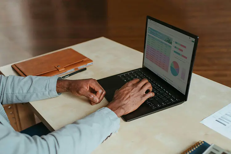 A person's hands typing on a laptop computer displaying data visualisations on the screen.